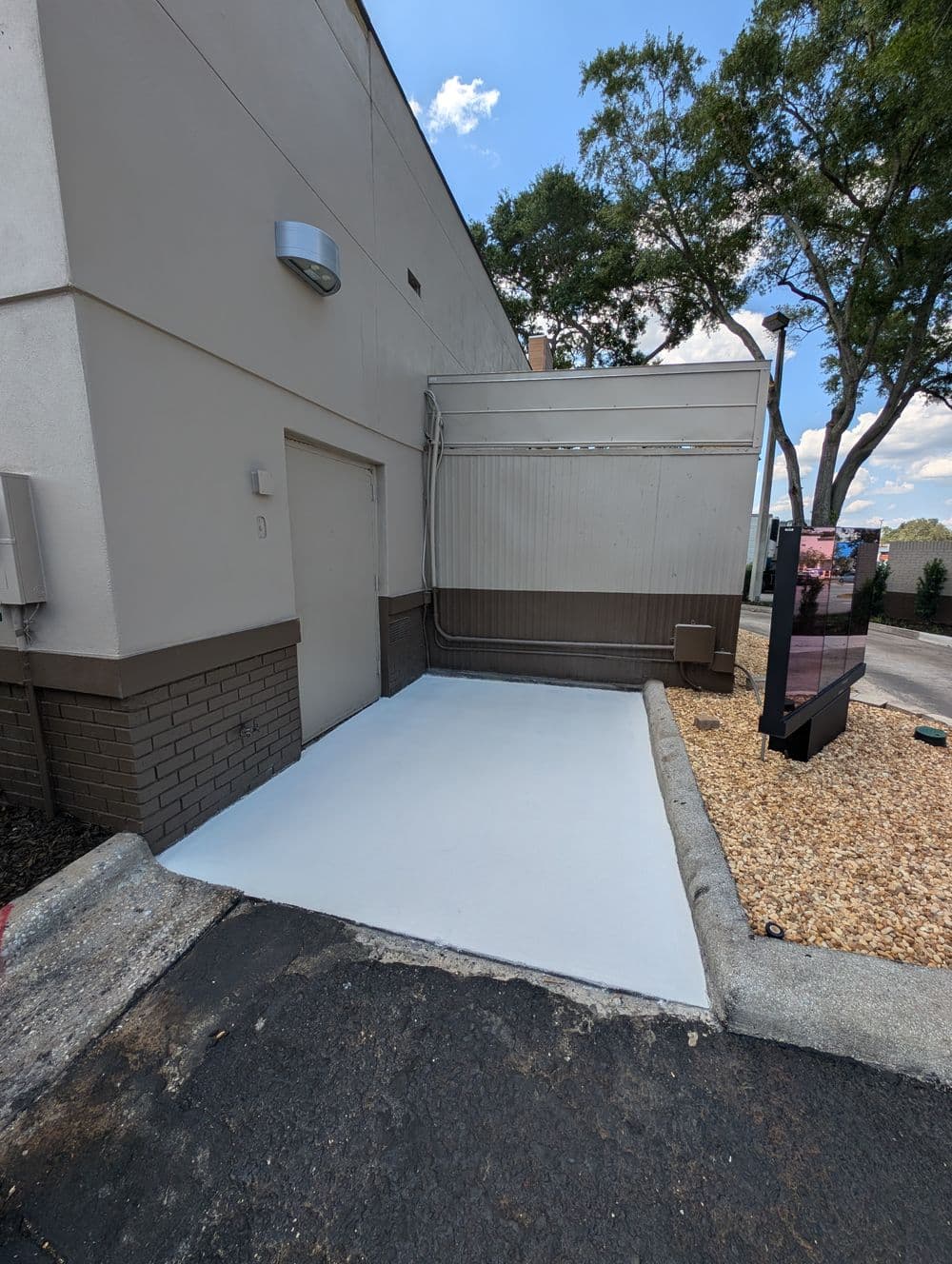 Freshly painted white concrete area beside a commercial building entrance, featuring landscaping.