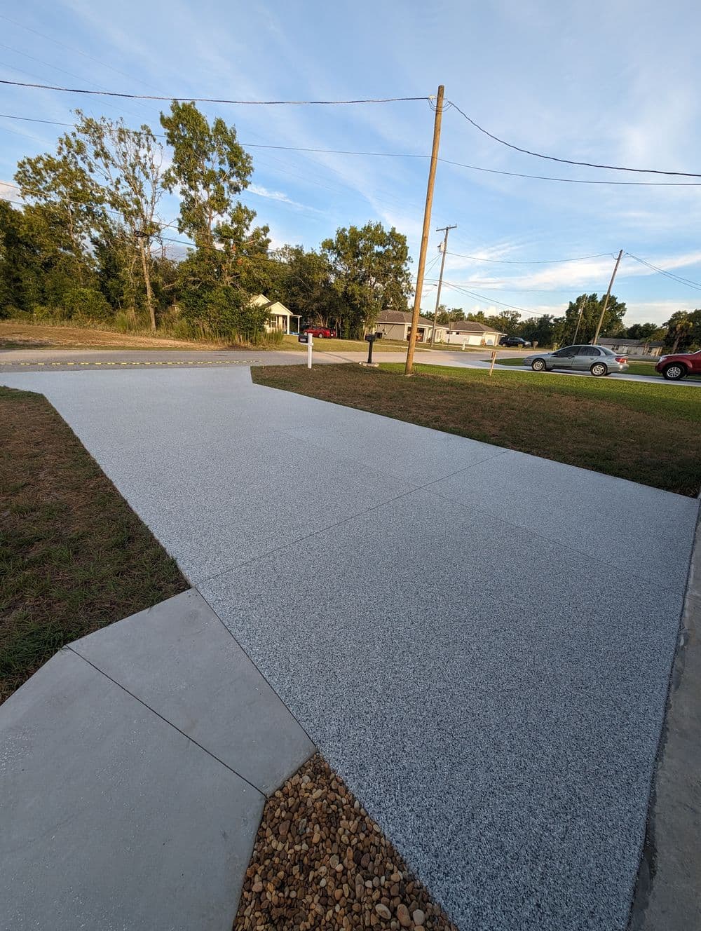 Newly installed decorative concrete driveway with gravel border and grassy area, under blue sky.