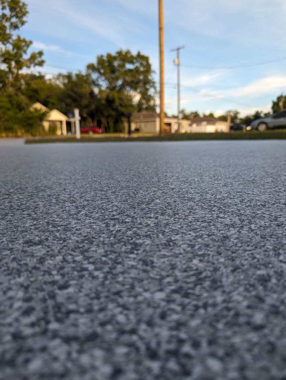 Close-up of textured pavement with trees and residential buildings in the background.
