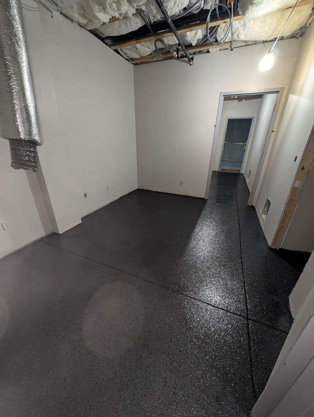 Freshly coated epoxy floor in a newly constructed room with exposed ceiling.