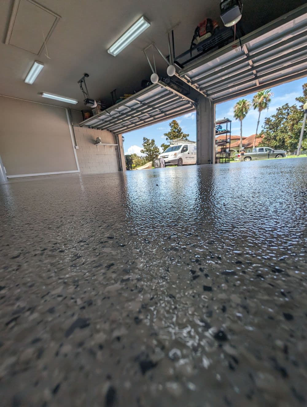 Shiny epoxy garage floor with open doors revealing sunny driveway and parked vehicles.