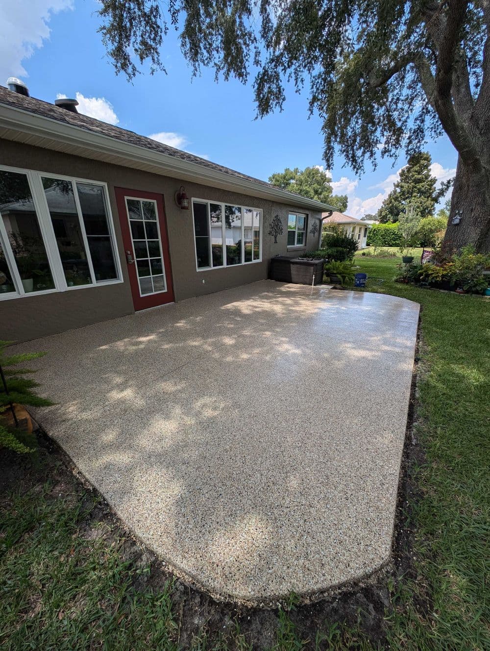 Patio with decorative stone finish, surrounded by greenery and trees, near home exterior.